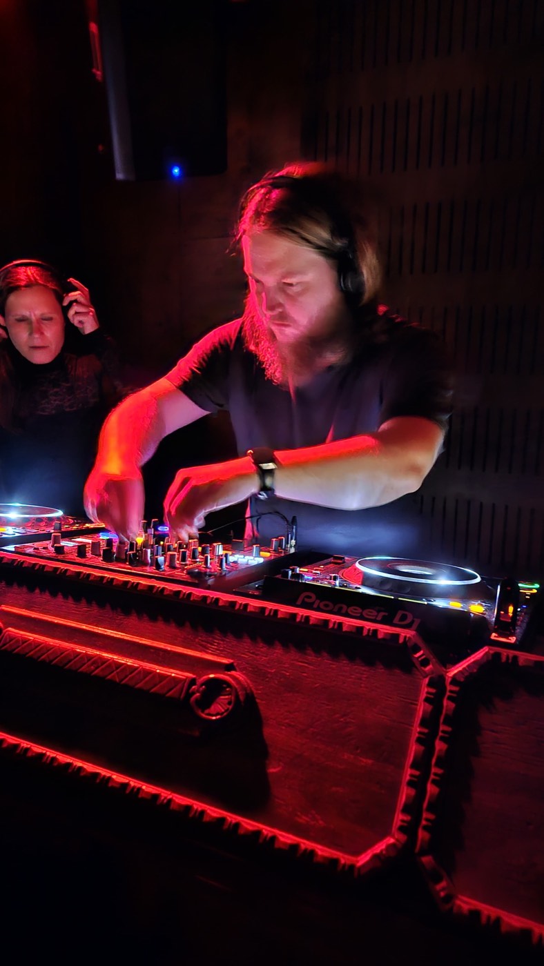 Brendo at the decks, lit red from the mixer.