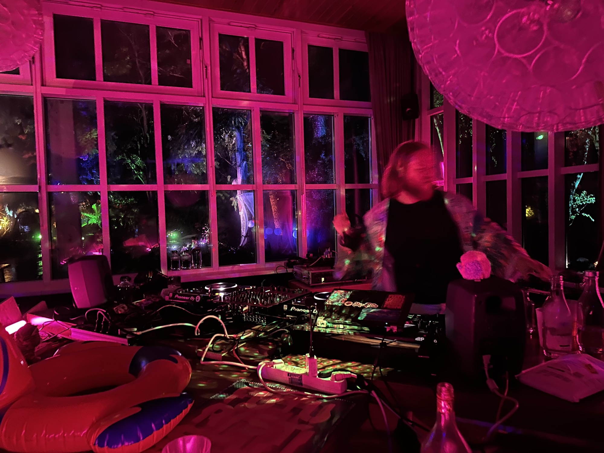 Brendo playing in a magenta-lit room, windows open onto a floodlit forest.